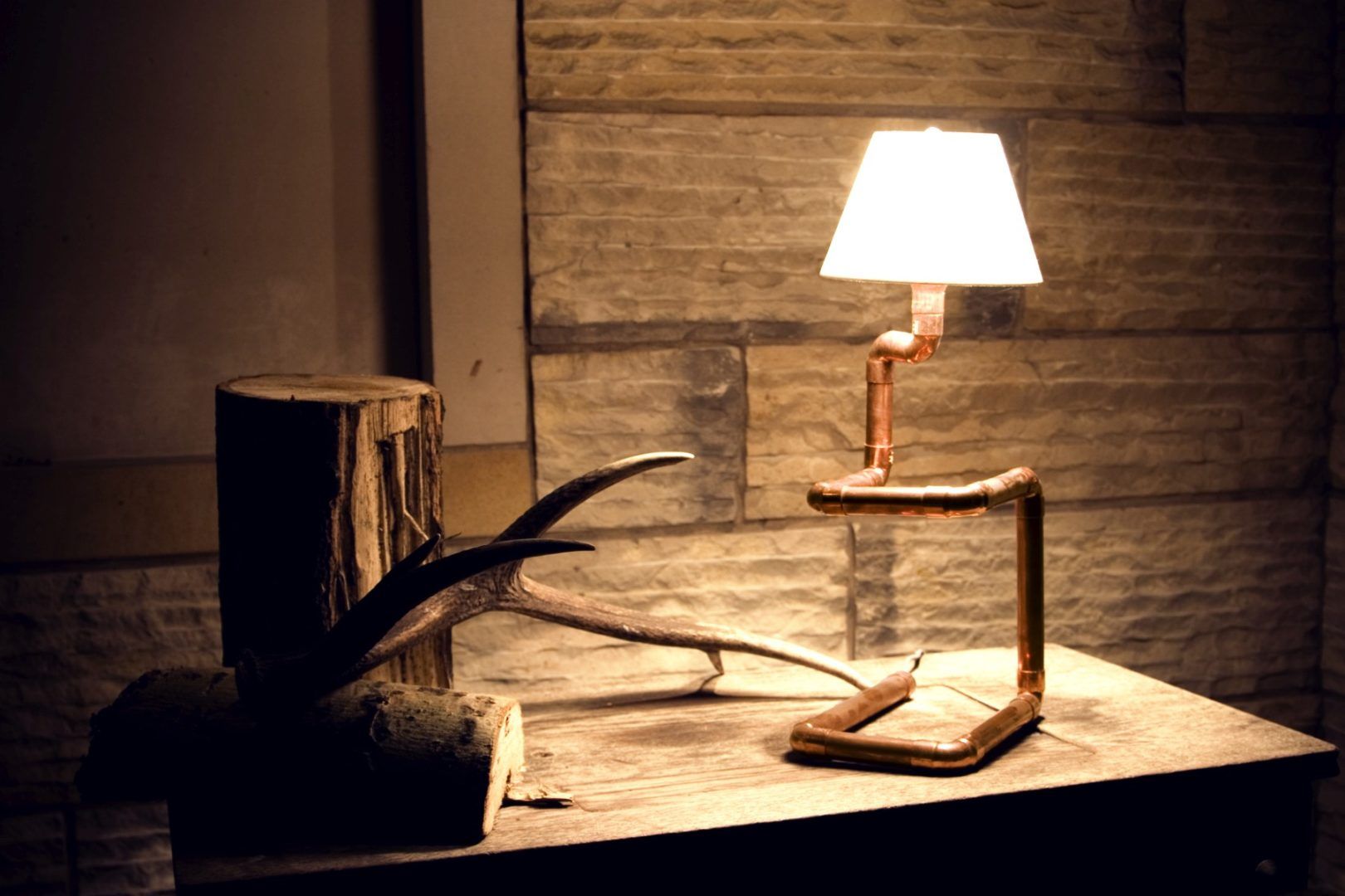 miedziana, asymetryczna lampa stołowa z białym abażurem - aranżacja w drewnie