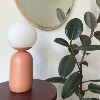 lampa stołowa terakota przy złotym lustrze i roślinie