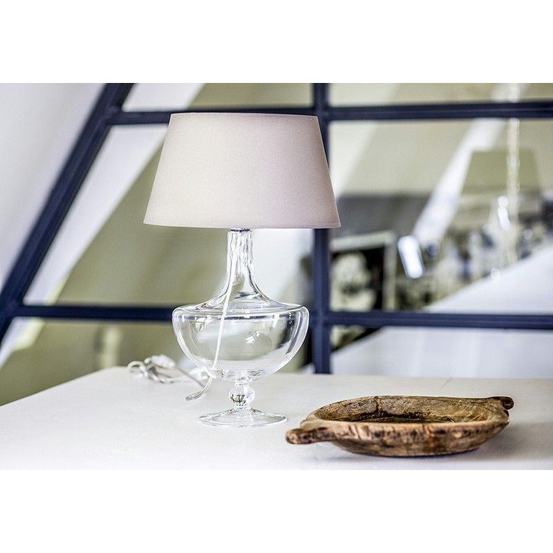 lampa stołowa ze szklaną, przezroczystą podstawą w oryginalnym kształcie i klasycznym, beżowym abażurem - aranżacja